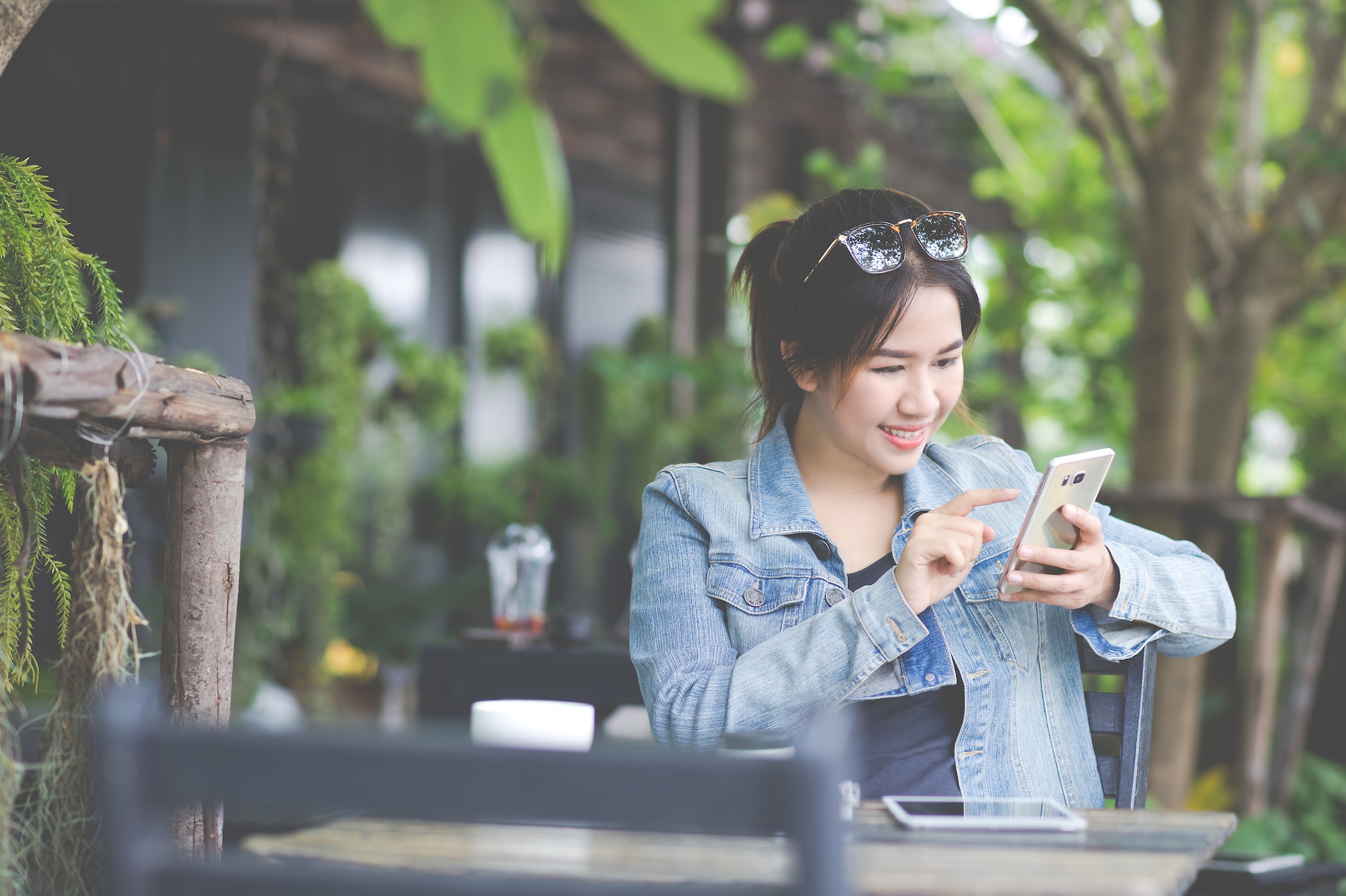 Young asian girl reading news at a coffee shop with a smartphone.